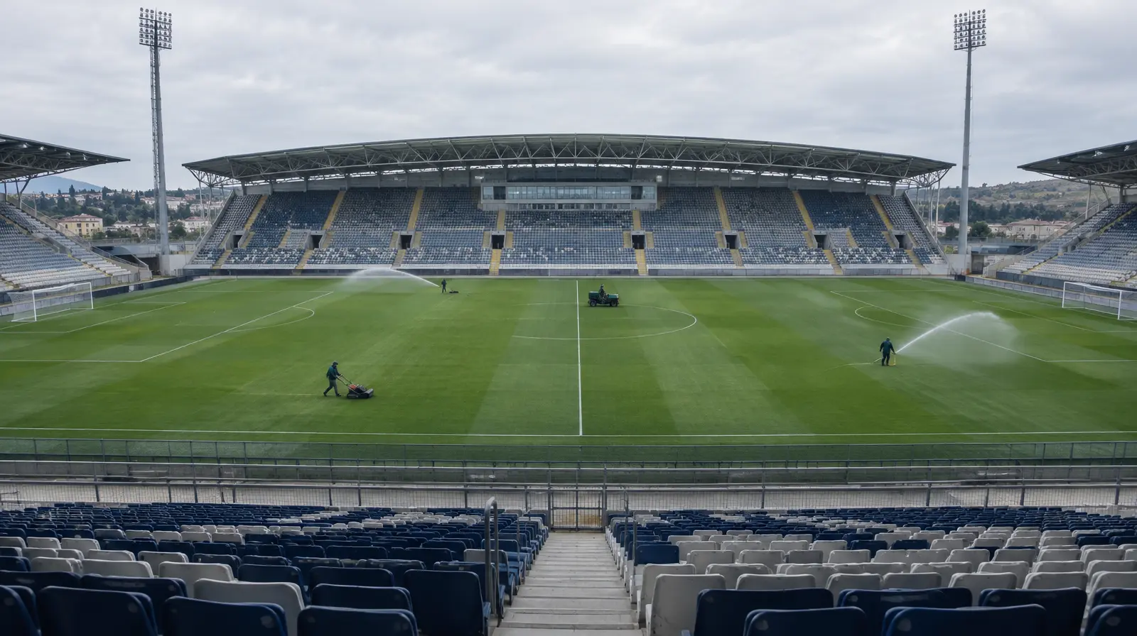 Tom fotbollsarena med vattnad plan och tomma läktare i dagsljus